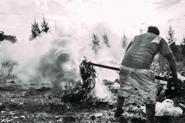 My neighbor Juan extracts copper by burning plastic cables recovered from the dump, while his son watches on (Patrick O'Hare, 2015)