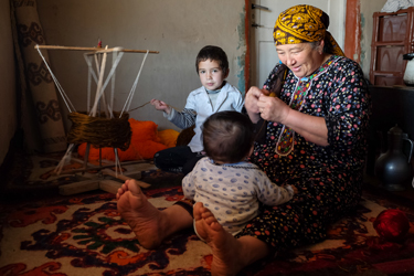 Entertaining the youngest grandson while her granddaughter helps spool synthetic yarn for alaja - colorful braids sold to city folks to adorn cars in the bridal party (Cara Kerven, 2016)