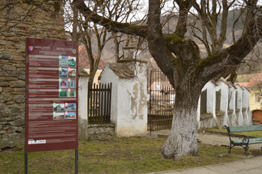 A board displaying the Romanian Ministry of Cultures regulations for the protection of architectural heritage, standing in front of a fortified Saxon Evangelical Church (Hugh Williamson, 2015)