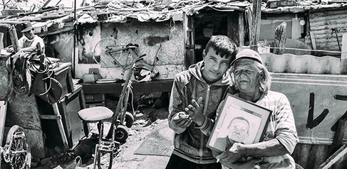 ‘Old’ Selva stands with her grandson and a picture of her own grandmother in front of her home