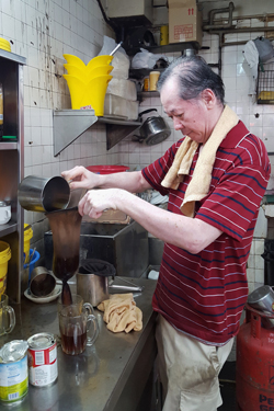Ting, aged 65 years, strains coffee through a sieve in the back kitchen of a kopitiam (Helen Jambunathan, 2017)