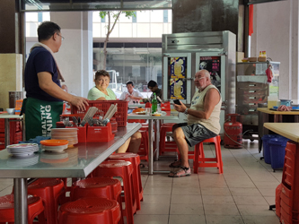 Mr Tay, on the left, interacts with a British tourist couple in his kopitiam (Helen Jambunathan, 2017)