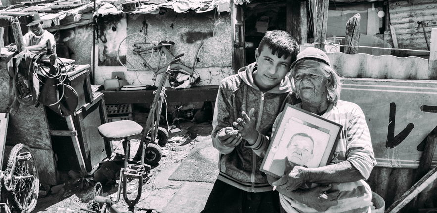 ‘Old’ Selva stands with her grandson and a picture of her own grandmother in front of her home (Patrick O'Hare, 2015)
