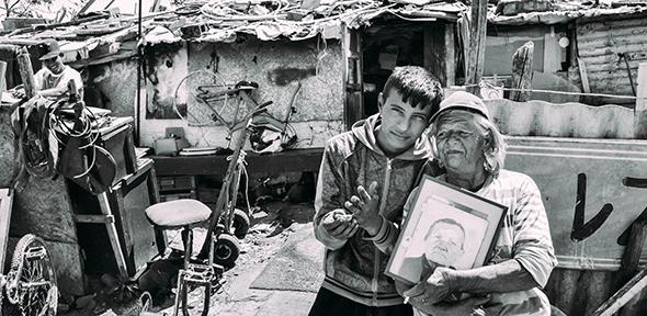 ‘Old’ Selva stands with her grandson and a picture of her own grandmother in front of her home